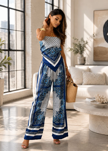 A woman models a strapless wide-leg jumpsuit with a blue, white, and black geometric and paisley print, standing in a bright, modern living room.