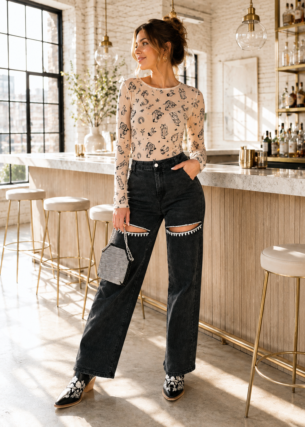 A woman stands in a bright, sunlit bar interior wearing a beige long-sleeve top with a black floral print, dark wide-leg jeans with distressed knee details, and black-and-white patterned shoes. She is holding a small gray handbag.