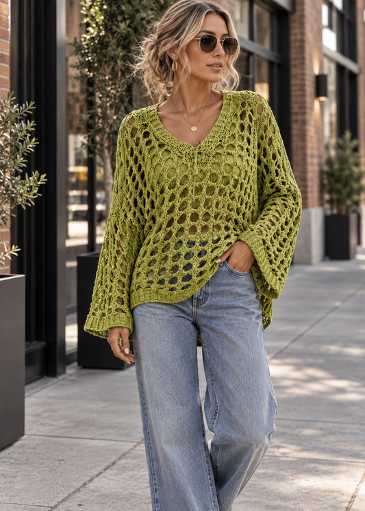 A woman wearing a chunky olive green open-knit long-sleeve sweater and light-wash wide-leg jeans, walking on a city sidewalk.