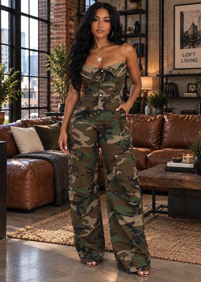 A woman modeling a strapless camouflage jumpsuit in a modern loft living room setting with brown leather sofas and brick walls.